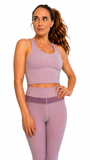 Woman wearing a matching purple sports bra and leggings set on a white background