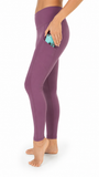 A side-profile view of a person wearing high-waisted purple leggings with a side pocket holding a turquoise phone, against a plain white background.
