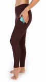 A person wearing dark brown leggings, shown from the waist down in profile, holding a small turquoise item in a side pocket against a plain white background.